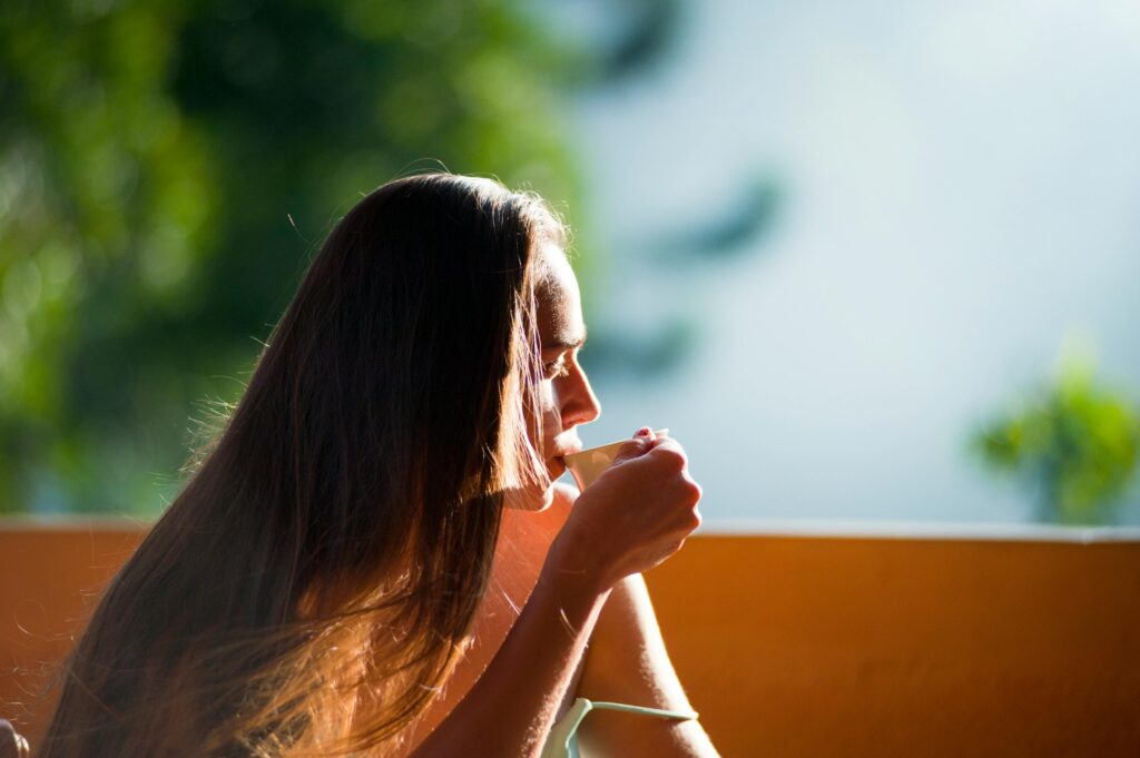 A woman peacefully sipping tea outdoors in the morning sunlight.