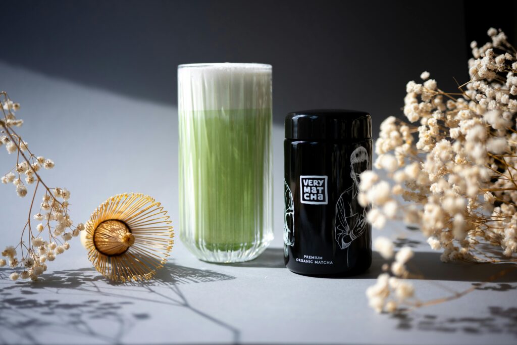 A stylish display of matcha latte with bamboo whisk and tea canister, adorned by soft florals.