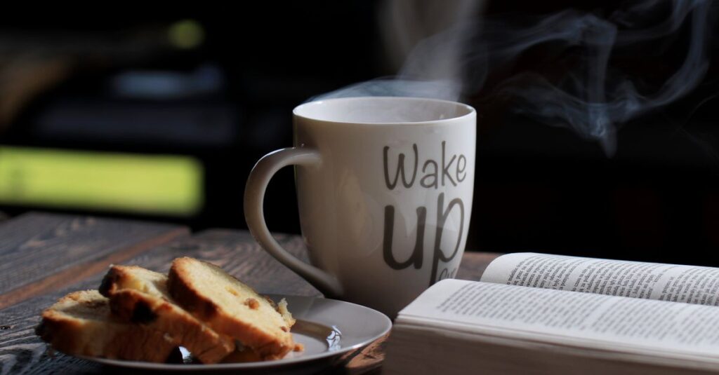 Steaming coffee with bread and an open book on a wooden table for a cozy morning.