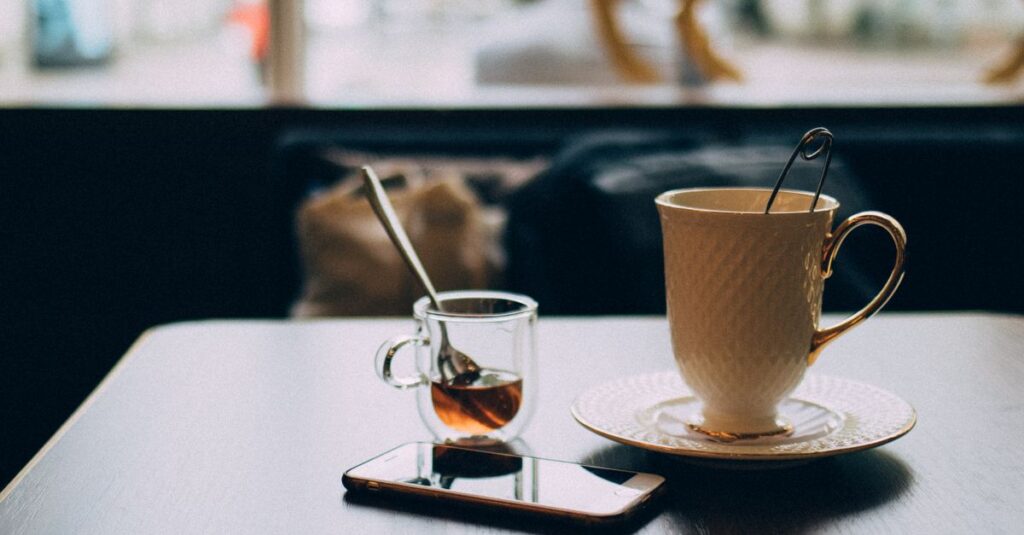 A warm and inviting coffee shop scene featuring a smartphone, tea cup, and small glass of syrup on a table.