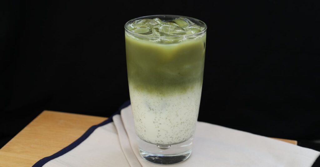 Refreshing iced matcha latte in a glass with milk on a wooden table.