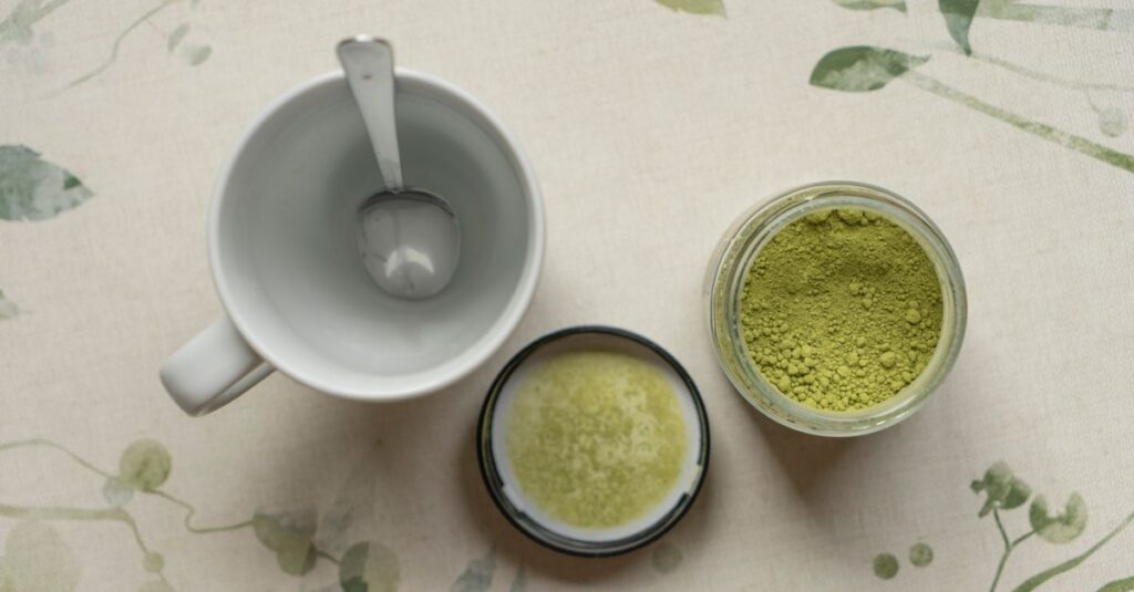 Top view of matcha powder in jar with empty cup on floral tablecloth.