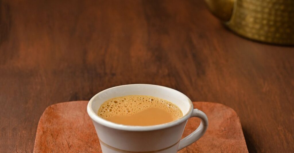 A cup of traditional Indian tea served on a wooden tray beside a brass kettle.