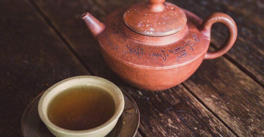 Clay teapot with intricate designs beside a cup of tea on rustic wood.