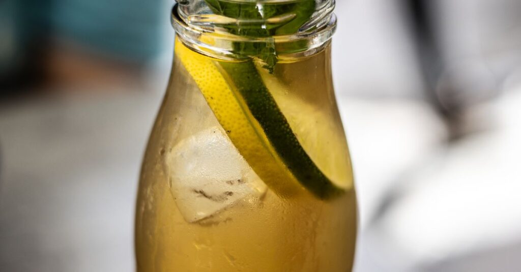 Cold refreshing lemonade in a bottle with mint leaves and a straw.
