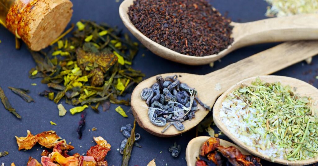 Assorted loose leaf herbal teas in wooden spoons on a flat lay composition, showcasing various colors and textures.
