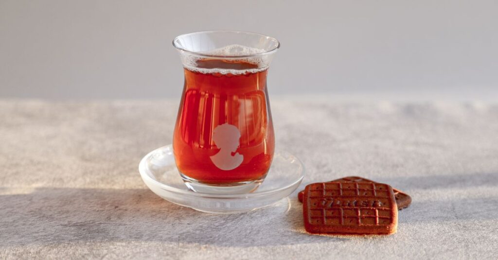 A glass of Turkish tea and a biscuit on a sunlit table, perfect for a serene afternoon break.