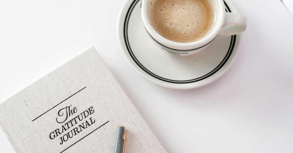 A gratitude journal beside a cup of coffee on a bright, minimalist table setting.