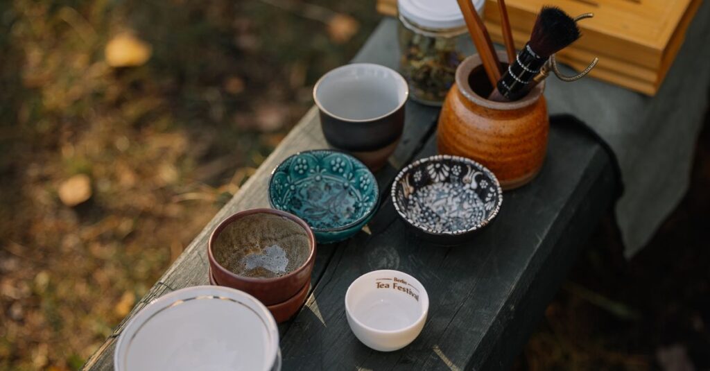 An assortment of rustic tea cups and bowls on a wooden table outdoors, capturing a serene setting.