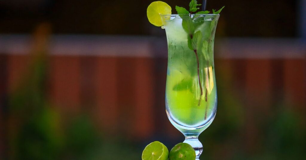 A vibrant mojito cocktail served with lime and mint leaves in a tall glass.