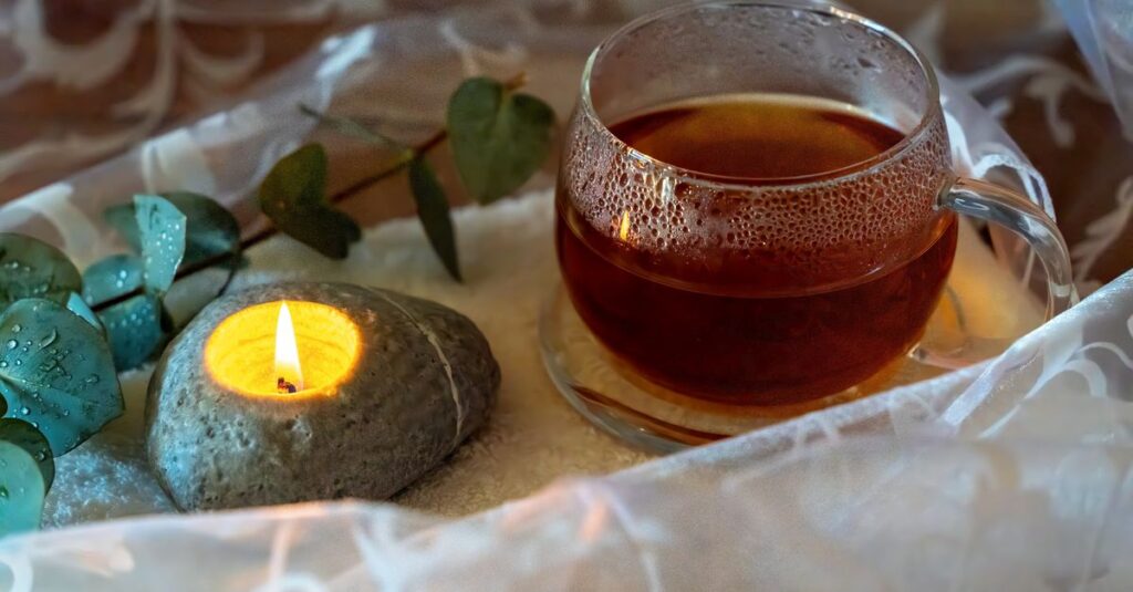 A peaceful tea setup with a glass teacup, stone candle, and eucalyptus leaves, perfect for relaxation.