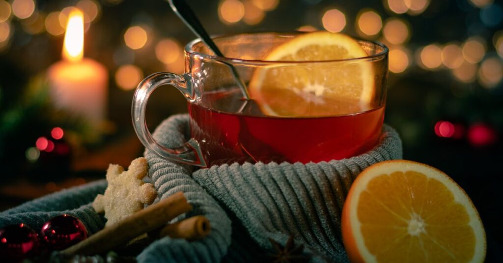 Warm cup of tea with oranges and cinnamon sticks, evoking winter magic beside candlelight.