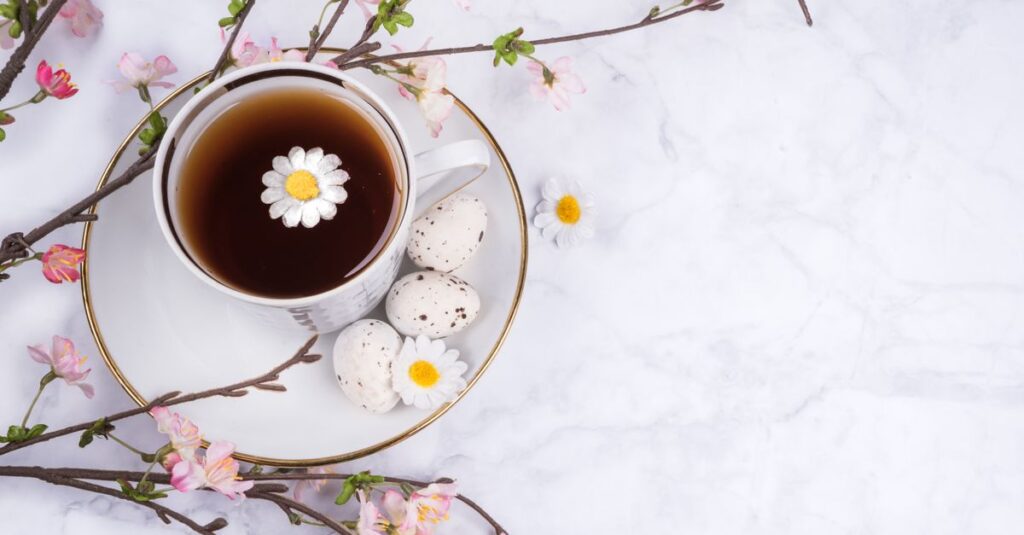 Cup of tea with cherry blossoms and Easter eggs on marble surface.