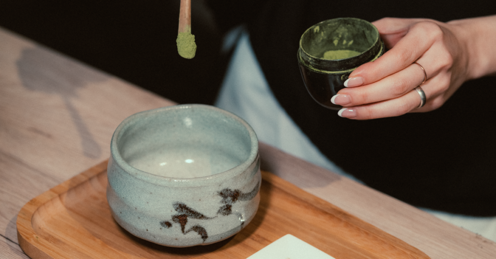 Close-up of hand preparing matcha tea with traditional Japanese utensils.