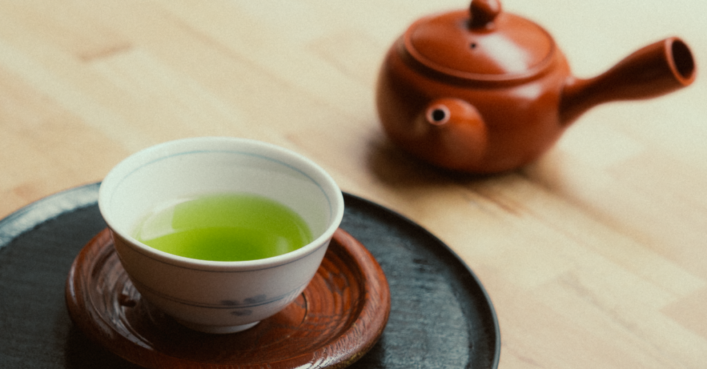 A cup of vibrant green tea and a clay teapot on wooden surface, capturing a calming essence.