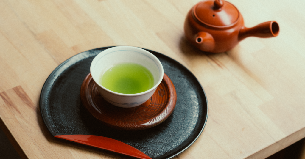 A serene setting featuring a cup of green tea with a traditional teapot on a wooden table.