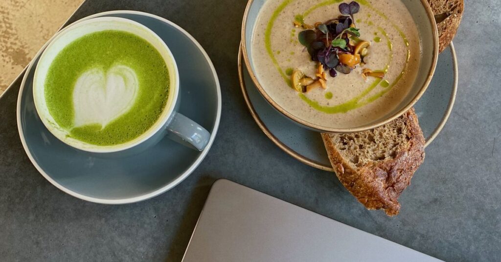 A cozy cafe scene with matcha latte and soup beside a laptop, perfect for work or relaxation.