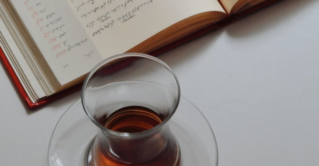 Open notebook with handwriting beside a glass of tea and laptop on a desk, ideal for study or work themes.