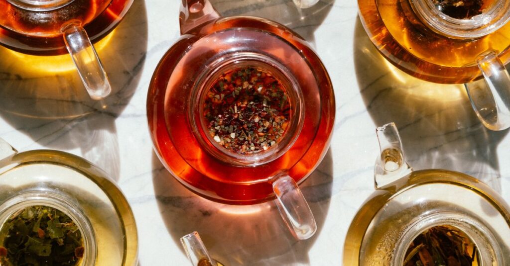 Top view of assorted herbal teas in glass teapots casting shadows on a marble surface.