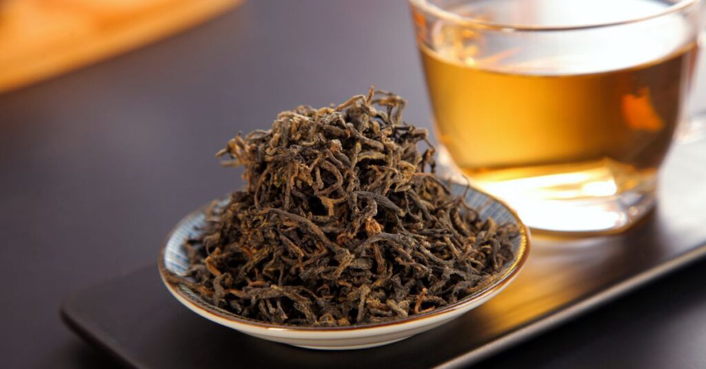 A close-up of loose leaf black tea beside a brewed cup, showcasing rich texture and warmth.