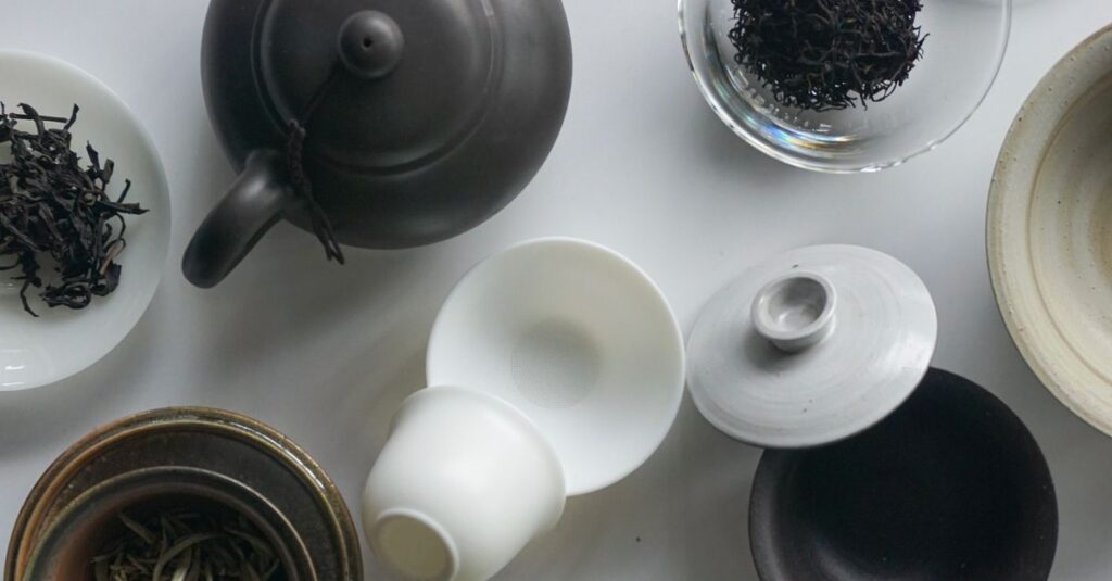 Elegant flat lay composition of a ceramic teapot and assorted loose tea leaves.