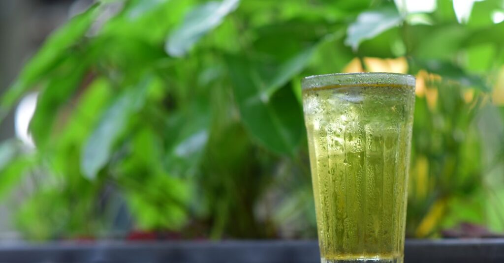 Chilled glass of matcha green tea with ice, set against a blurred green background.