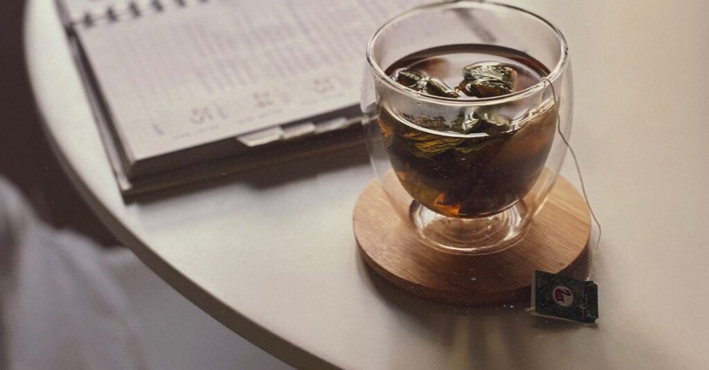 A warm glass of mint tea on a wooden coaster, sitting beside an open planner.