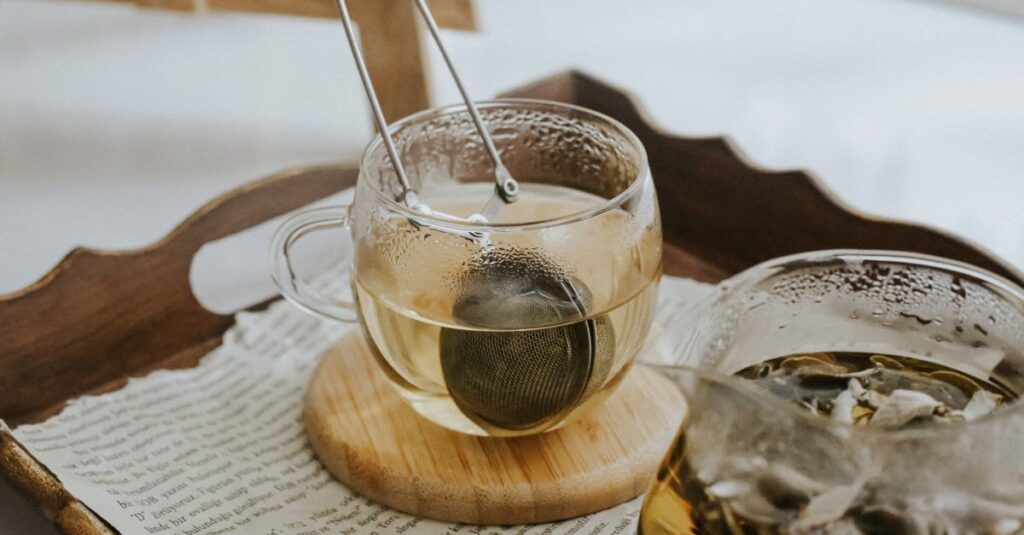 A warm, cozy scene showcasing glass teacups with tea infuser on a tray with scattered papers.