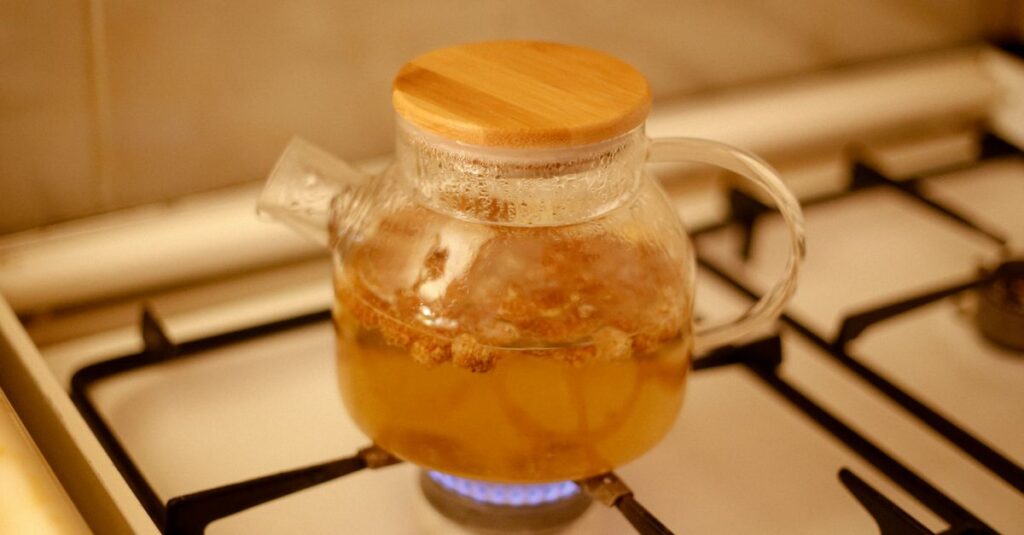 A glass teapot brewing herbal tea on a kitchen gas stove with a warm ambiance.