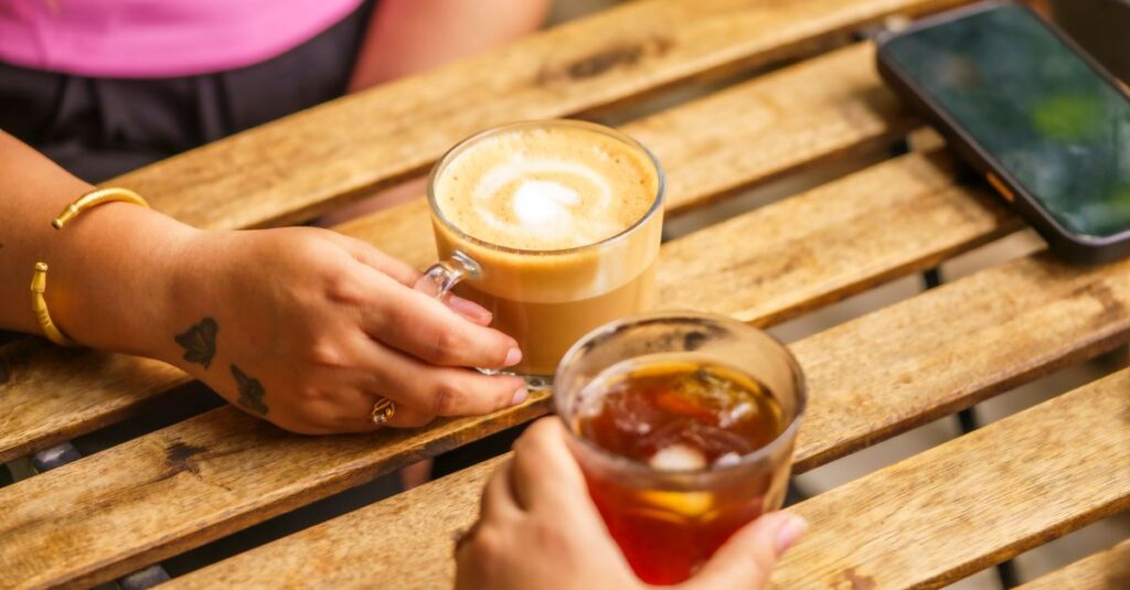 Two people enjoying coffee and iced tea on a wooden table outdoors. Casual and relaxed atmosphere.