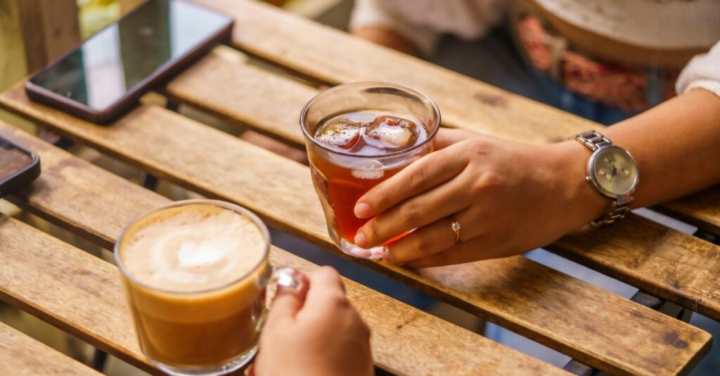 Two people enjoying coffee and tea at a wooden table outdoors.