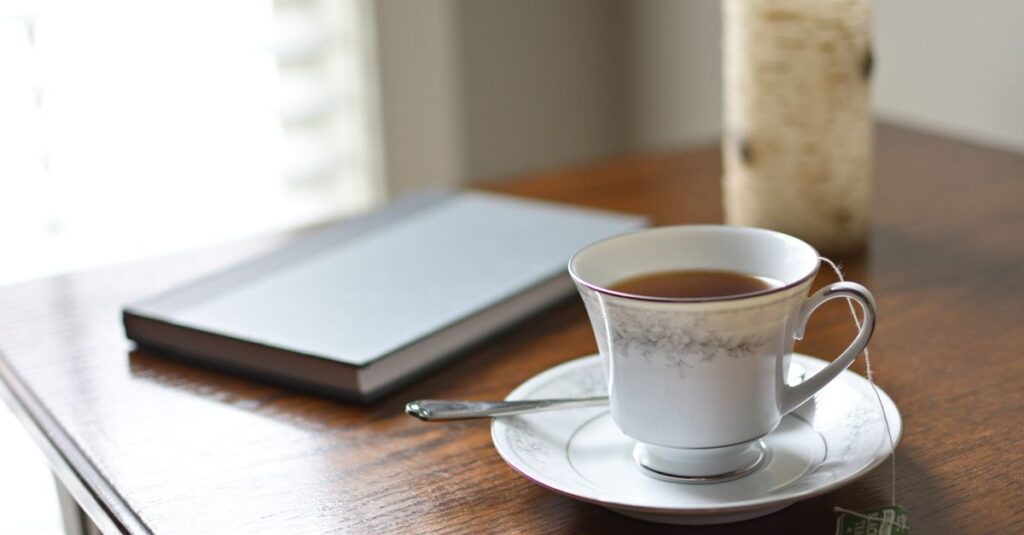 A serene morning scene with a teacup, journal, and candle on a wooden table, perfect for relaxation and reading.