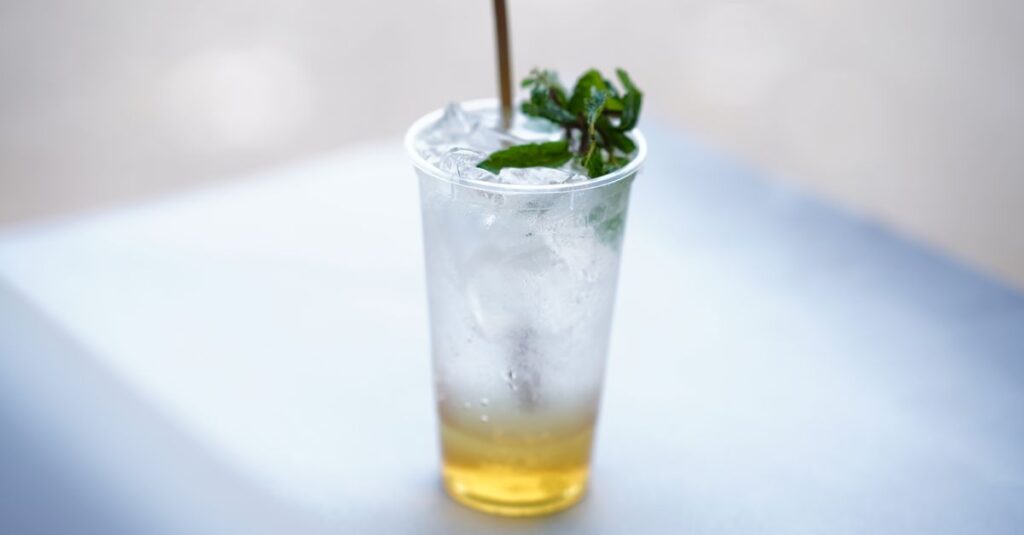 Chilled iced mint lemonade with mint garnish in a clear plastic cup on a sunny day.