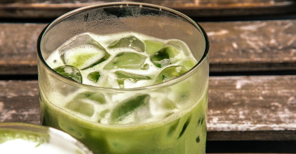 A close-up of a refreshing iced matcha latte on a rustic wooden table, highlighting its natural green color and fresh appeal.