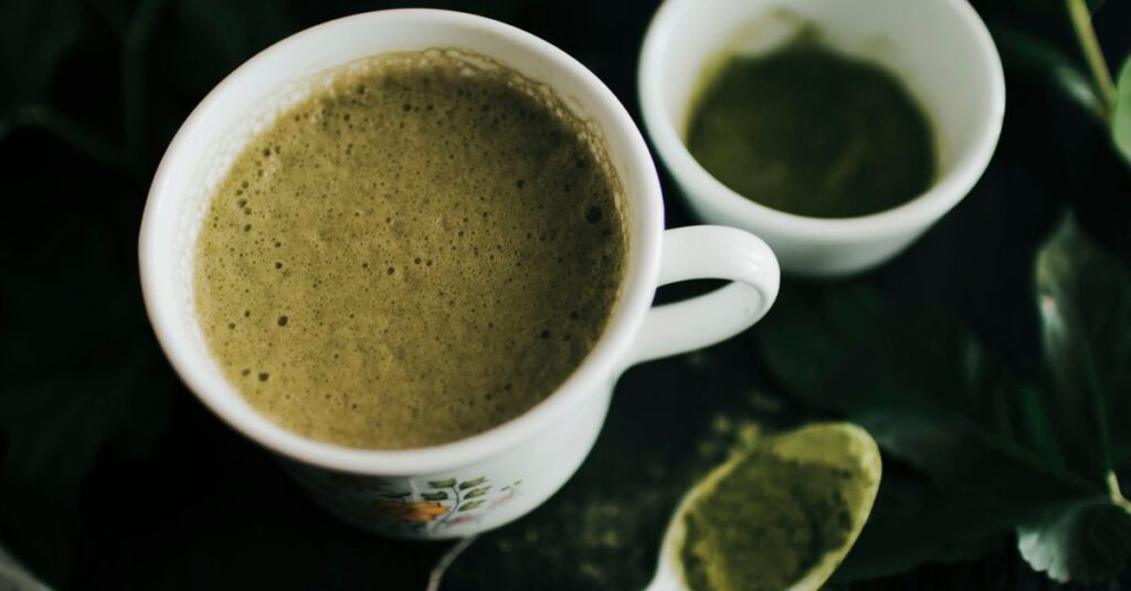 Close-up of a frothy matcha latte in a ceramic cup with matcha powder on spoon.