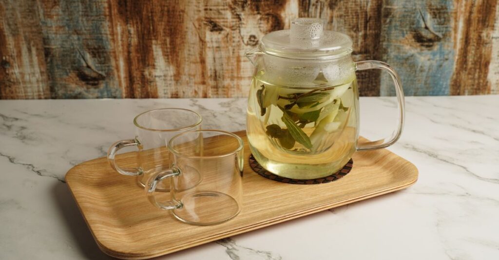 Clear glass teapot with herbal tea and matching cups on a wooden tray.