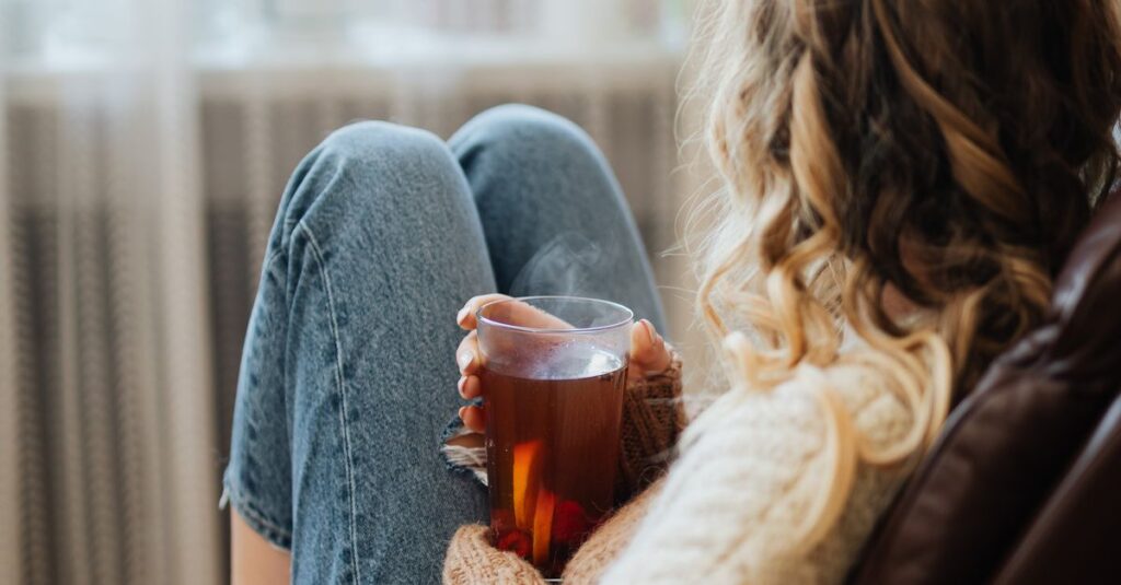A woman enjoys a warm cup of tea while relaxing by a window indoors.