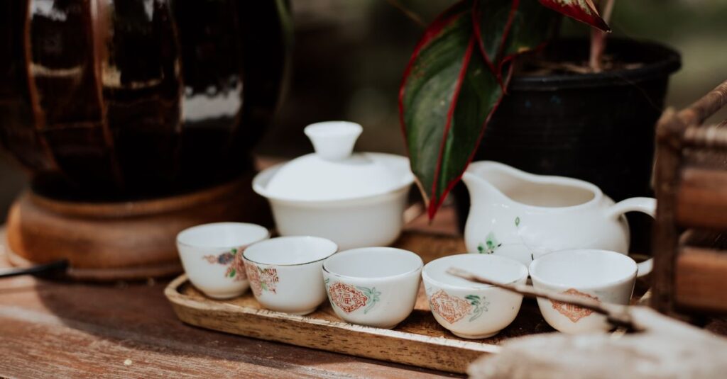 Rustic tea set with porcelain cups and teapot on a wooden tray, accented by floral patterns and a houseplant in the background.