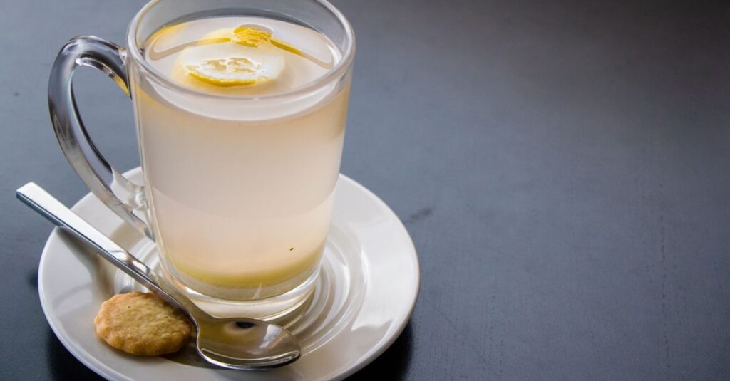 Refreshing lemon infused water in clear glass with biscuit and saucer, perfect for a health-focused lifestyle.