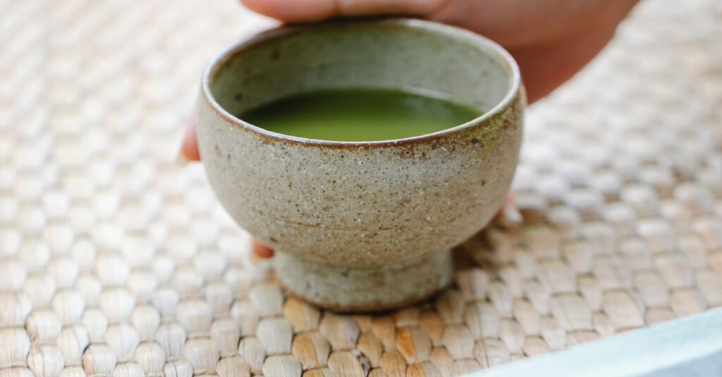 From above of crop anonymous person serving ceramic bowl with matcha in daylight