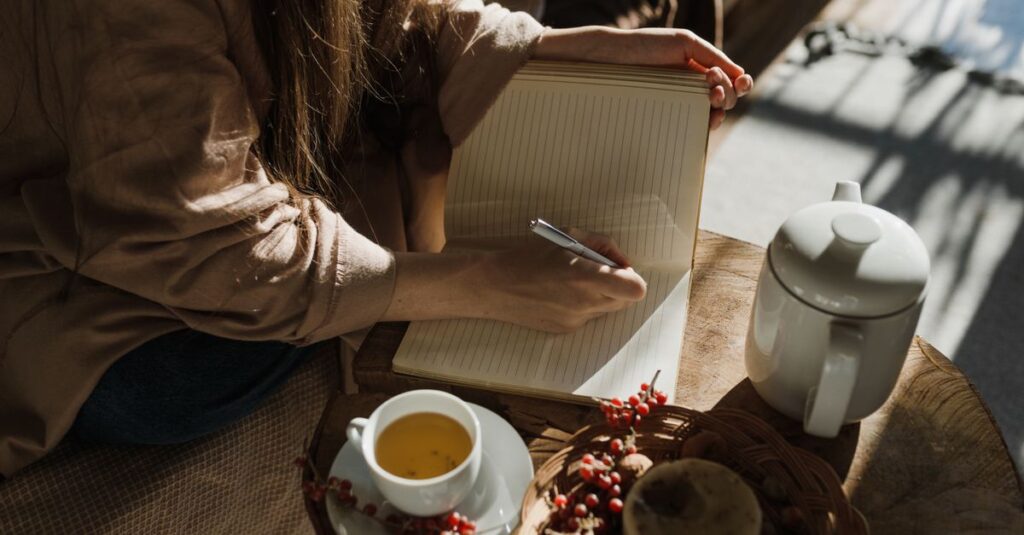 A person writes in a notebook while enjoying tea in natural light. Cozy and serene ambiance.