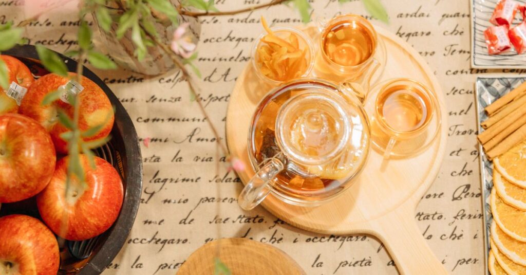 Elegant tea arrangement with fresh apples and spices on a script-patterned tablecloth.