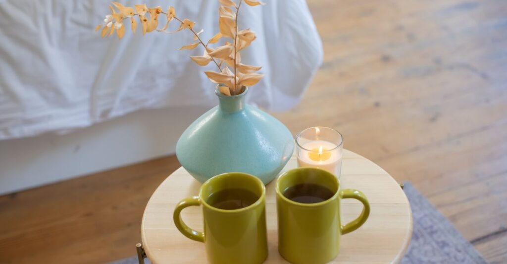 Two green mugs on a table with a vase and candle, evoking a cozy indoor atmosphere.
