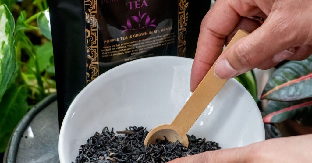 Close-up of hands scooping purple tea leaves with wooden scoop in a white bowl. Ideal for product photography.