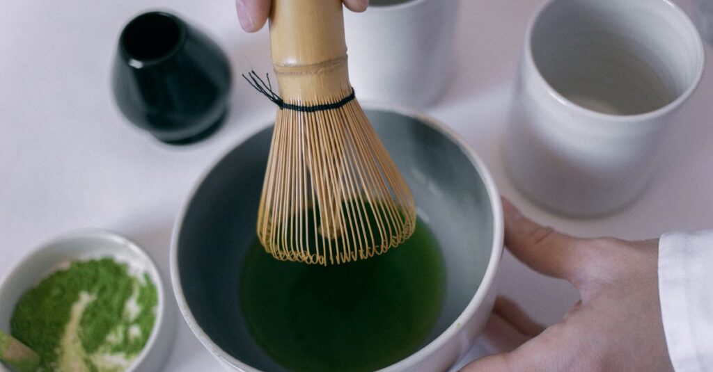 Close-up of hands using a bamboo whisk to prepare matcha tea in a ceramic bowl.