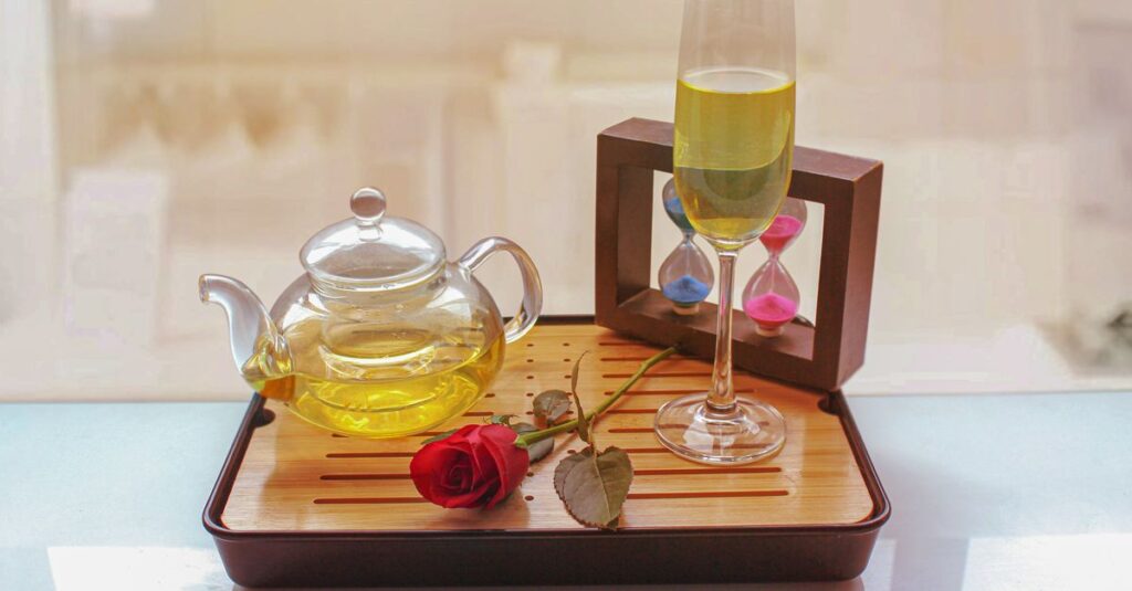 A charming arrangement of green tea in a glass teapot with a rose on a tray.