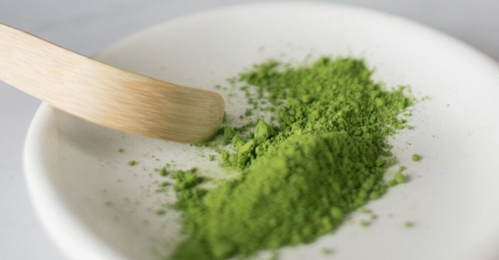 Closeup of dry green food coloring for cooking on white plate with wooden spatula on white surface in kitchen