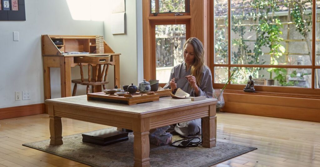 Woman enjoying a peaceful tea ceremony in a serene, sunlit room with a wooden interior.