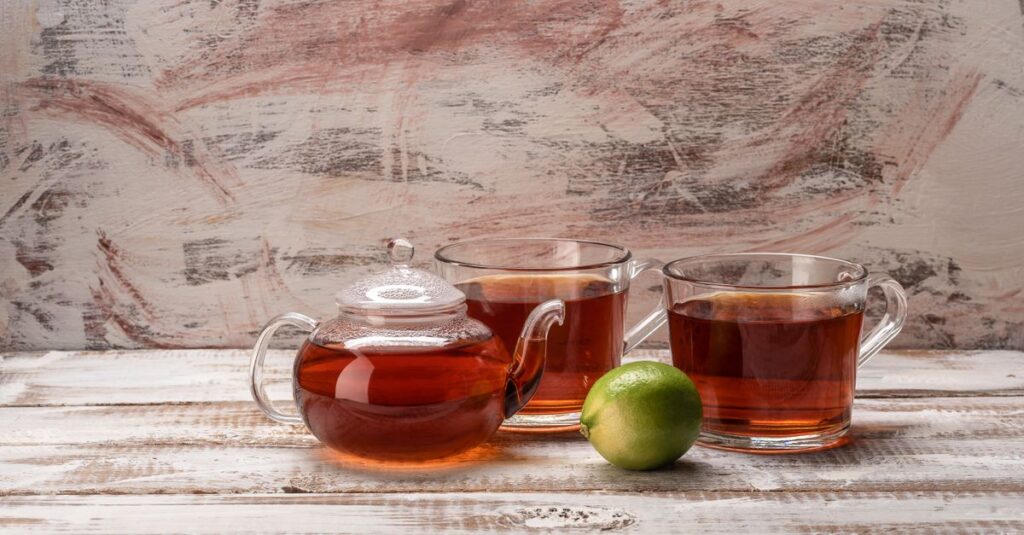 Elegant glass teapot and cups filled with tea on a wooden surface with a fresh lime.