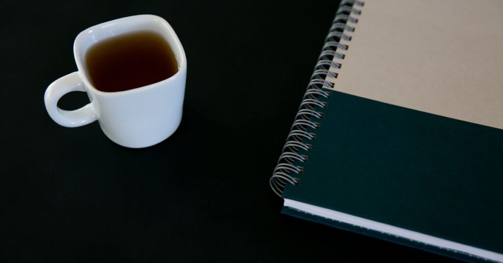 Close-up of a white tea cup and a spiral notebook on a black background. Perfect for themes of productivity and simplicity.